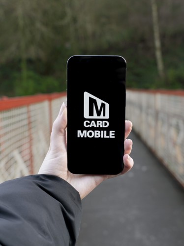 Hand holding smartphone displaying MCard Mobile app logo
